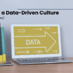 Building a Data-Driven Culture - webinar review (text) bookend in shape of a person holding up several small books, laptop with the word "data" written across the screen. Both sit on a desk.